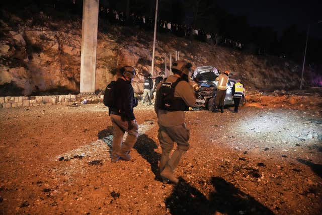 Israeli security forces inspect a destroyed car after a missile launched from Iran struck a road in Jerusalem