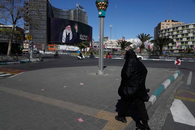 A woman crosses almost deserted square with a billboard at rear showing a portrait of the late Iranian Supreme Leader Ayatollah Ali Khamenei, who was killed in the U.S.–Israeli military campaign, in Tehran on Tuesday 