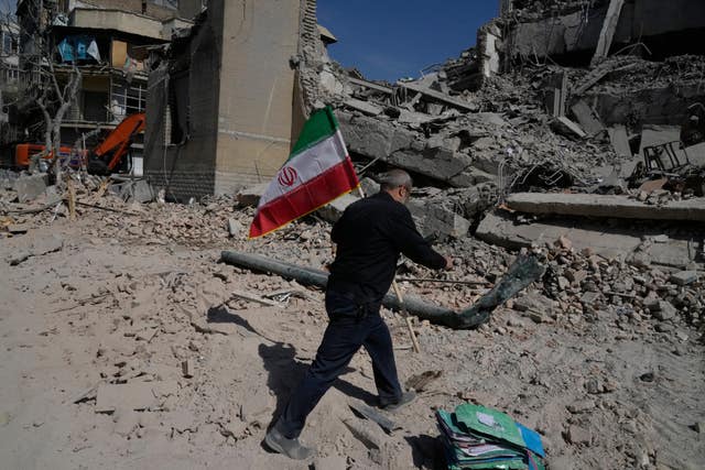 A man carries an Iranian flag to place in the rubble of a police facility struck during the US–Israeli military campaign in Tehran 