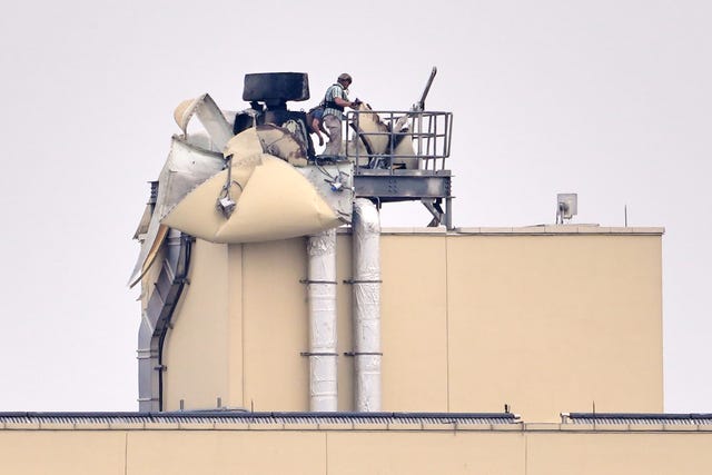 A man inspects damage on the top of a building
