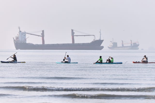 People paddle along the shoreline as cargo ships are anchored in the Strait of Hormuz off Bandar Abbas, Iran