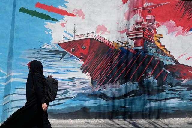 A woman walks past a mural depicting a US aircraft carrier under missile attack in Tehran