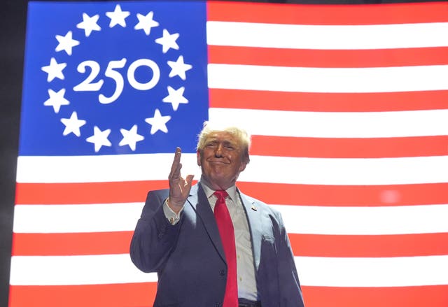 Donald Trump standing in front of a US flag incorporating the number 250 inside a circle of 13 stars