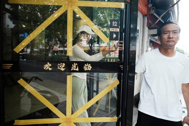 A man walks by glass doors taped up in preparation for the anticipated Typhoon Bavi