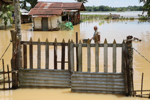 A man wades through floodwater near his submerged house in Assam, India