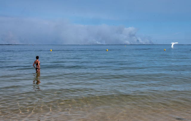 A woman watches smoke rising on the horizon from a beach in Arcachon as wildfires rage in western France