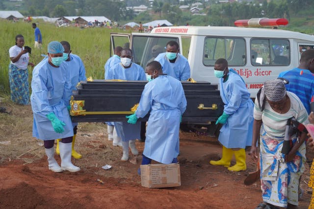 People dressed in protective gear unload a coffin 
