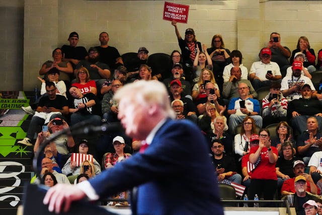 Donald Trump speaking in the foreground as audience members listen to him in the background