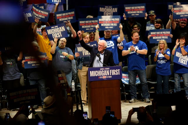 Bernie Sanders raising his fist in the air while standing behind a lectern at a campaign rally in Grand Rapids, Michigan